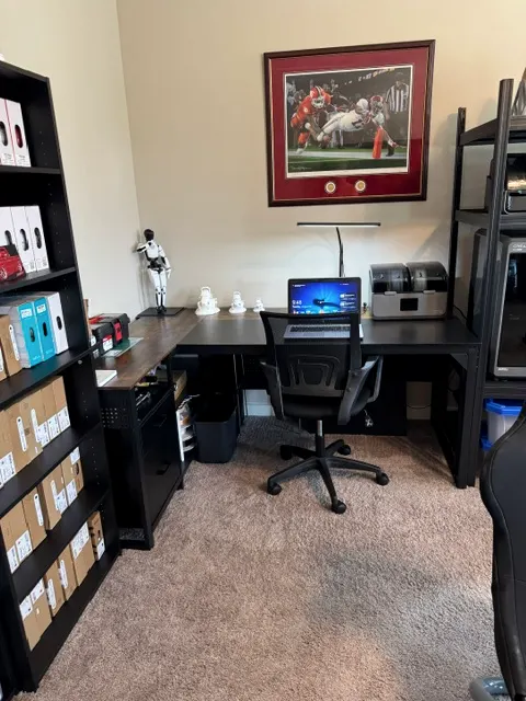 The assembly desk: a laptop, two filament dryers and finished prints waiting on the bench, with shelves of filament alongside.
