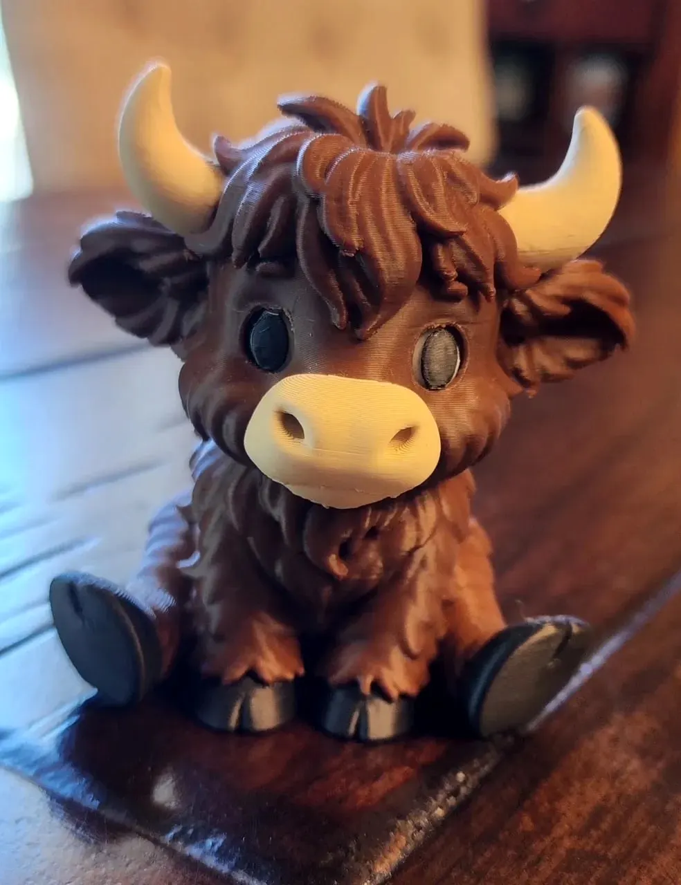 Small sitting Highland calf figure with textured brown fur, cream horns and muzzle, and black hooves