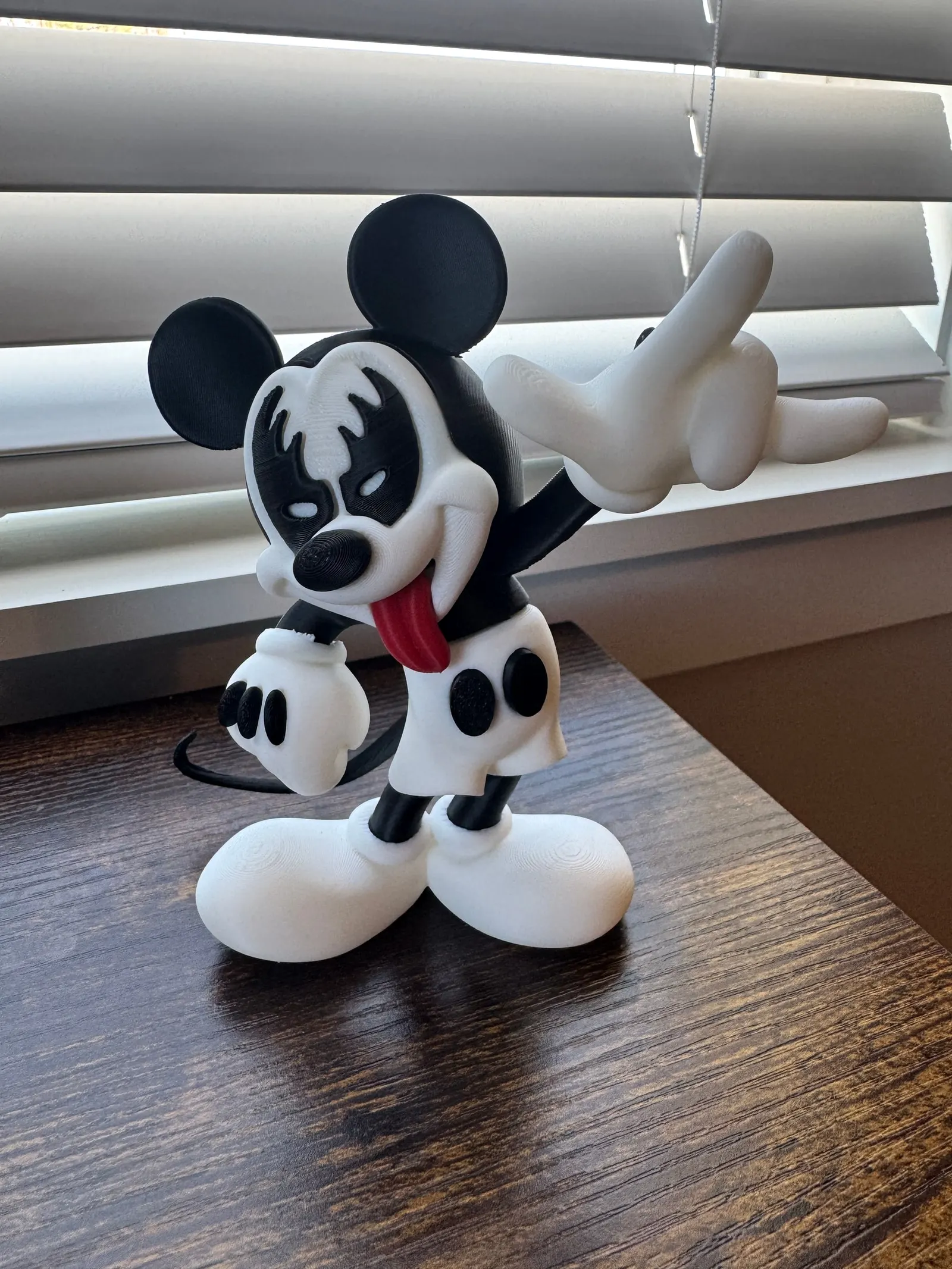 Cartoon mouse figure in rock-band face paint making a rock hand sign